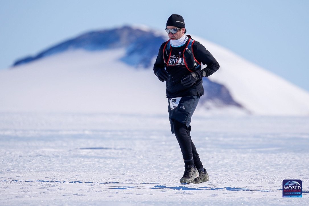 Greg Yaghmai running across the snow in Antarctica with a mountain ridge behind him