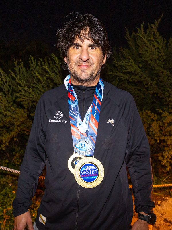 Greg Yaghmai wearing a KultureCity jacket with his World Marathon Challenge finisher medals around his neck