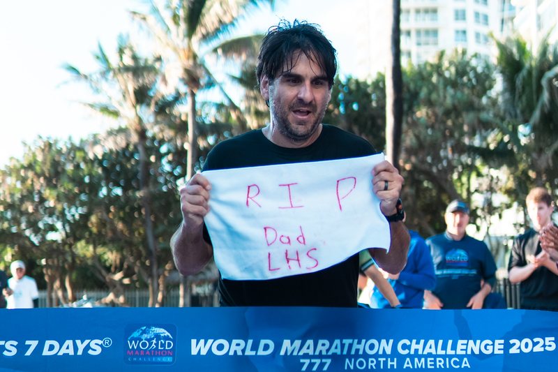 Greg Yaghmai breaking the tape at the Miami finish line holding a handwritten sign